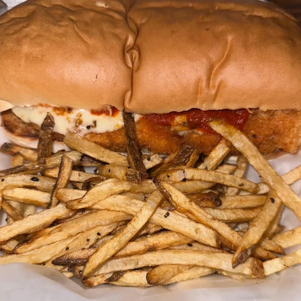 A chicken parmesan sandwich with melted cheese and red sauce, served with a side of fries.